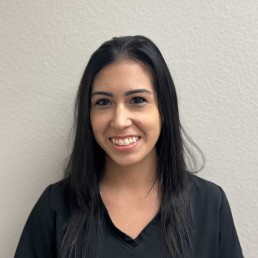 Meet Our Team: A woman with long, straight dark hair and a black top smiles in front of a plain light-colored wall.