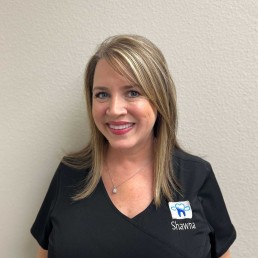 Meet Our Team: A smiling woman with straight blonde hair wears a black scrub top with a dental logo and